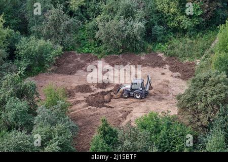 Der Bagger bereitet den Boden auf dem Feld im Wald unter den Bäumen für die Landschaftsgestaltung und Landwirtschaft, Draufsicht - Moskau, Russland, 24. August 2021 Stockfoto