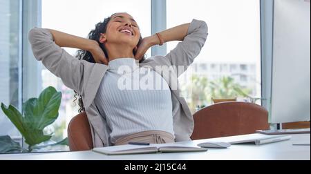 Einen weiteren erfolgreichen Tag durchstehen. Aufnahme einer jungen Geschäftsfrau, die während der Arbeit in einem Büro mit den Händen hinter dem Kopf eine Pause einnahm. Stockfoto
