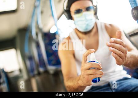 Hübscher blonder Kerl im Unterhemd, der mit öffentlichen Verkehrsmitteln mit Schutzmaske, Sonnenbrille und Kopfhörern reist, respektiert epidemiologische Maßnahmen und Stockfoto