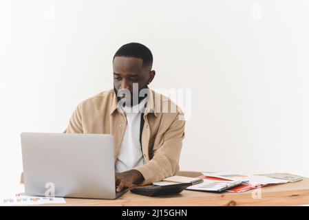 Fokussierter afroamerikanischer Mann, der von zu Hause aus am Laptop arbeitet. Der freie Programmierer arbeitet am Tisch Stockfoto