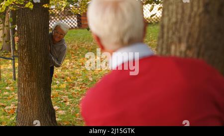 Gealtertes kaukasisches Paar, das sich von hinter den Bäumen anschaut, fällt Mann wird von hinten fotografiert, konzentrieren sich auf die Frau voller Schuss Parkhintergrund. Hochwertige Fotos Stockfoto