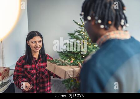 Der afroamerikanische Mann überrascht seine kaukasische Frau mit einem Weihnachtsgeschenk. Interracial paar Konzept. Hochwertige Fotos Stockfoto