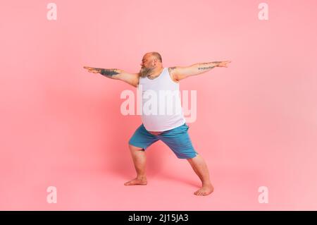 Lustiger Mann mit Bart in Yoga-Position auf Studio rosa Hintergrund Stockfoto