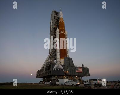 Der Mond steigt hinter der NASA-Rakete Space Launch System (SLS) mit der Orion-Sonde an Bord auf einem mobilen Trägerrakete auf, während er zum ersten Mal am Donnerstag, dem 17. März 2022, im Kennedy Space Center der NASA in Florida zum Launch Complex 39B ausrollt. Vor dem Artemis I-Flugtest der NASA werden die vollständig gestapelte und integrierte SLS-Rakete und die Orion-Raumsonde im Launch Complex 39B einer Nassprobe unterzogen, um die Systeme zu verifizieren und Countdown-Verfahren für den ersten Start zu üben. Bildnachweis: (NASA/Aubrey Gemignani) Stockfoto