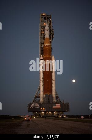 Der Mond steigt hinter der NASA-Rakete Space Launch System (SLS) mit der Orion-Sonde an Bord auf einem mobilen Trägerrakete auf, während er zum ersten Mal am Donnerstag, dem 17. März 2022, im Kennedy Space Center der NASA in Florida zum Launch Complex 39B ausrollt. Vor dem Artemis I-Flugtest der NASA werden die vollständig gestapelte und integrierte SLS-Rakete und die Orion-Raumsonde im Launch Complex 39B einer Nassprobe unterzogen, um die Systeme zu verifizieren und Countdown-Verfahren für den ersten Start zu üben. Bildnachweis: (NASA/Aubrey Gemignani) Stockfoto