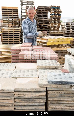 Mann in Handschuhen, der Pflasterplatten auf Paletten im Lager aufbocken kann Stockfoto