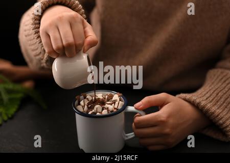 Nahaufnahme, Eine Frau in einem gemütlichen Pullover, die einen Schokoladensirup auf eine heiße Schokolade mit Marschmalow gießt. Stockfoto