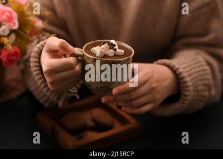 Frau in einem warmen Pullover schlürft heiße dunkle Schokolade mit marmelow Bonbons. Warm und gemütlich. Stockfoto