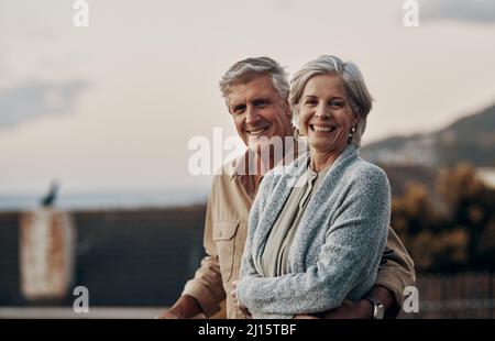 Wir freuten uns, gemeinsam ein weiteres neues Jahr zu feiern. Beschnittenes Porträt eines liebevollen reifen Paares, das lächelt, während es auf einem Balkon steht Stockfoto