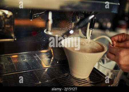 Nur ein Schuss Milch. Nahaufnahme einer nicht erkennbaren Person, die tagsüber heiße Milch in eine Tasse Kaffee im Restaurant gießt. Stockfoto