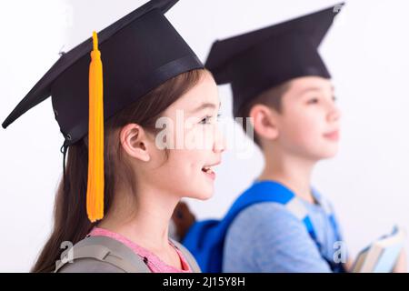 Seitenansicht des glücklichen Jungen und Mädchens in der Abschlusskappe mit Büchern Stockfoto