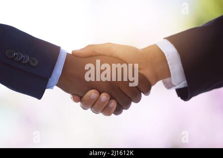 Münzen und Bargeld für Ausgeglichenheit und Schwung. Aufnahme von zwei unverkennbaren Geschäftsleuten, die sich vor einem verschwommenen Hintergrund die Hände schüttelten. Stockfoto