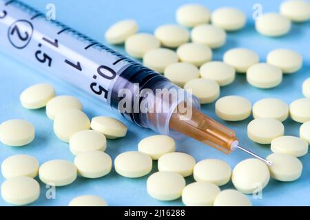 Spritze mit gelben Pillen auf blauem Hintergrund. Medizinisches Konzept. Stockfoto