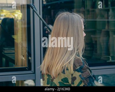 kaukasisch blondes jugendliches Soldatenmädchen an einem Kontrollpunkt mit einem Gewehr und einer camogrünen Militäruniform während eines Konflikts in einem Kriegsgebiet Stockfoto