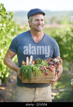 An der Güte der Natur festhalten. Ein lächelnder, reifer Bauer hält einen Korb mit frischen Produkten. Stockfoto