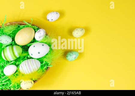 Osternest mit Eiern und Federn auf gelbem Hintergrund. Blick von oben. Platz für Text, Beschriftung. Osterkonzept. Stockfoto