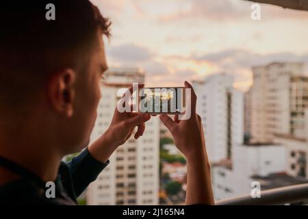 Ich muss das festhalten, bevor die Sonne untergeht. Ausgeschnittene Aufnahme eines nicht erkennbaren Mannes, der draußen mit seinem Handy ein Foto von der Stadt machte. Stockfoto