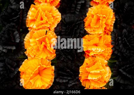 Blumen auf Denkmal. Künstliche Blumen an der Gedenkstätte. Orangefarbene und schwarze Blütenknospen. Kranz auf Grab. Stockfoto