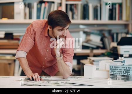 Junge Erwachsene kaukasischen Architekten arbeiten und denken am Tisch mit Projekt, Zeichnungen Blaupause und Haus Layout im Architekturbüro. Stockfoto