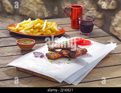 Köstliche Lammkoteletts, serviert auf einem Backpapier, wie die griechische Tradition sagt, zusammen mit gebratenen frischen Kartoffeln und Rotwein, Stockfoto