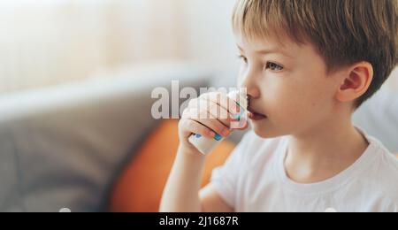 Der kleine Junge verwendet Nasenspray, während er auf der Couch sitzt Stockfoto