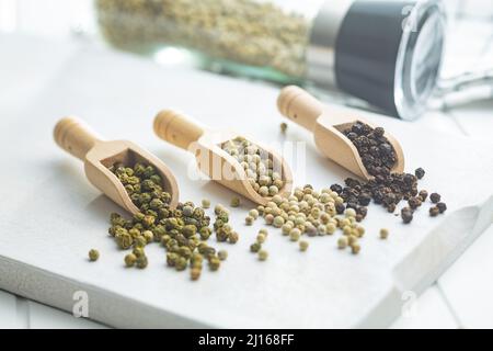 Drei verschiedene Arten von Pfeffergewürz. Grüner, weißer und schwarzer Pfefferkorn in den Holzschaufeln. Stockfoto