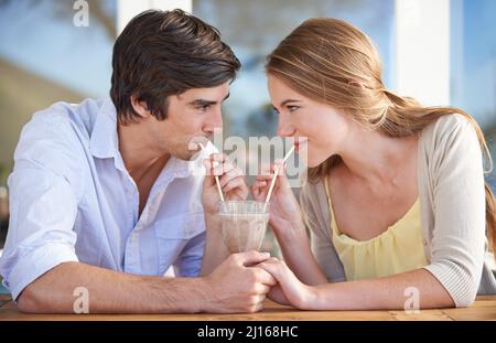 Teilen eines Milchshake. Ein junges Paar, das sich einen Schokoladenmilchshake teilt, während es ein Date hat. Stockfoto