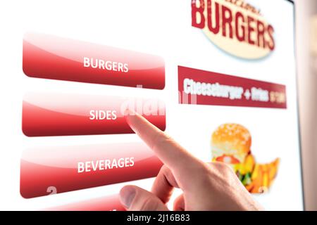 Selbstbedienung und Kiosk im Restaurant. Fastfood-Touchscreen, digitaler Verkaufsautomat. Mann, der ein elektronisches Menü verwendet und eine Burger-Mahlzeit kauft. Stockfoto