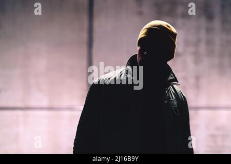 Mann mit dunklem Gesicht. Unbekannter Fremder, Stalker, Dieb oder Gangster im Schatten. Geheime verborgene Identität einer geheimnisvollen Person. Gefährlicher Verbrecher in Jacke. Stockfoto