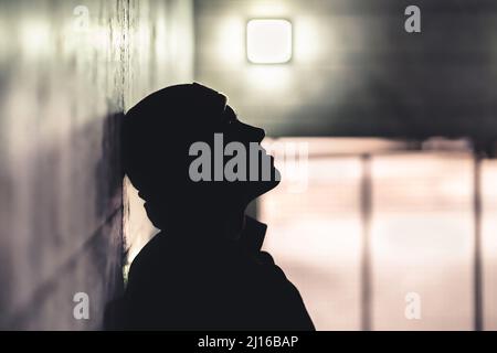 Ernsthafter trauriger Mann im Dunkeln. Depressive ängstliche Person leidet an Trauma, Einsamkeit oder Drogenabhängigkeit. Obdachlose wurden mit Scham nach Fehler ausgestoßen. Stockfoto