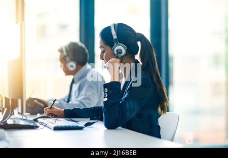Kunden zu helfen, ist das, was sie tun. Eine kurze Aufnahme von zwei Kundendienstmitarbeitern bei der Arbeit in ihrem Büro. Stockfoto