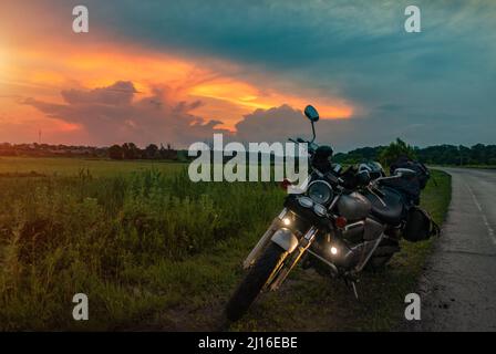 Retro Motorrad steht auf der Straße bei Sonnenuntergang Hintergrund. Motorradreise Stockfoto