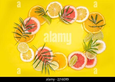 Bunte Flatlay von Zitrusfrucht Scheiben und tropischen Palmblättern. Orange, Grapefruit, Zitrone, Limette helle, hochfarbige Scheiben auf gelbem Hintergrund. Summe Stockfoto