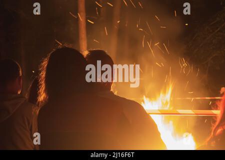 Das Paar steht umarmt vor dem Feuer. Liebevolles Paar aschert sich am Feuer Stockfoto