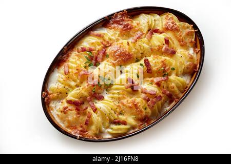 Draufsicht auf appetitliches Gratin mit gebackenen Kartoffelscheiben und knusprigen Speckstücken, die in einer ovalen Pfanne auf weißem Hintergrund gebacken werden Stockfoto