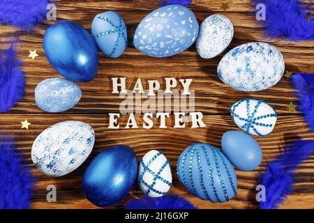 Frohe ostern, Schriftzug auf stilvollem Holztisch, Hintergrund. Blaue und weiße Eier gibt es überall. Bunte Ostereier, Draufsicht. Copyspace. Stockfoto