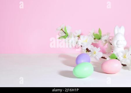 Ostereier, rosa, grün und lila, auf einem weißen Betontisch, neben bunnie und Blumen, auf einem rosa Hintergrund. Pastelltöne. Stockfoto