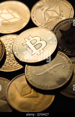 Nahaufnahme eines goldenen Bitcoins in einem Stapel, unter anderem verschiedener digitaler Kryptowährungen. Stockfoto