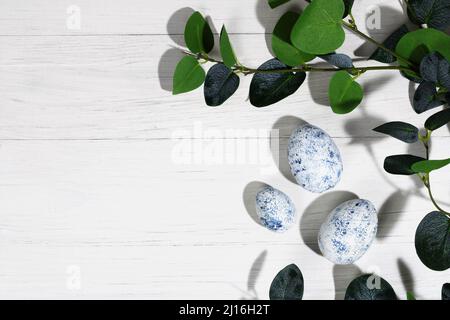 Sammlung von Ostereiern. Hühnereier von blauer Marmorfarbe liegen auf einem weißen Holzhintergrund mit Ästen. Kreative Grußkarte mit Ostern. Fram Stockfoto