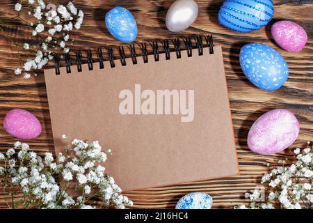 Bastelheft für Text auf angesagtem Holz Öko Hintergrund mit rosa und blauen Ostereiern und weißen Blumen. Draufsicht. Speicherplatz kopieren Stockfoto