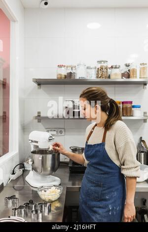 Weibliche Konditorin, die beim Kochen in der Backküche einen elektrischen Mixer verwendet. Stockfoto