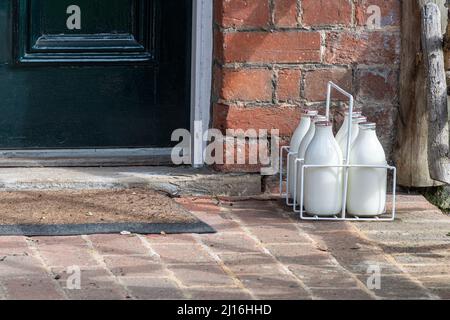 Sechs Flaschen Milch (Pint Milch), die von einem Milchmann geliefert und in einer Kiste vor der Haustür eines britischen Hauses zurückgelassen wurden Stockfoto