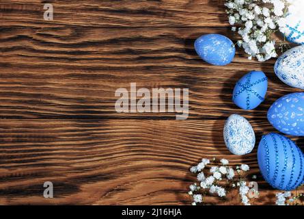 Blau und weiß, mit Strasssteinen, Ostereier auf einem trendigen gelben Holzhintergrund mit Blumen verstreut. Das Minimalkonzept von Ostern. Draufsicht. E Stockfoto