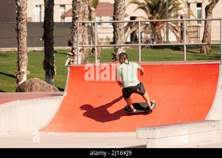 Mann reitet Skateboard im städtischen Street Skatepark. Lässiger Typ in Shorts und T-Shirt. Stockfoto