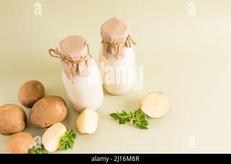 Zwei Flaschen umweltfreundliche Kartoffelmilch aus allen Arten pflanzlicher Milch auf beigem Hintergrund mit Kartoffelknollen Stockfoto