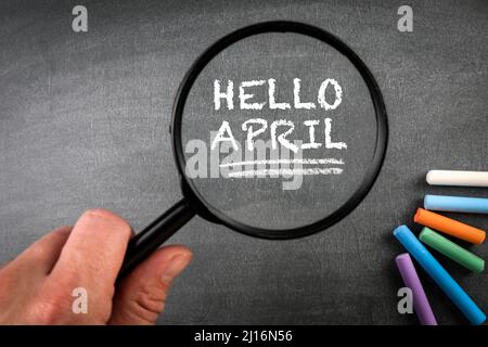 Hallo April. Farbige Kreidestücke und eine Lupe auf einem Tafelhintergrund. Stockfoto