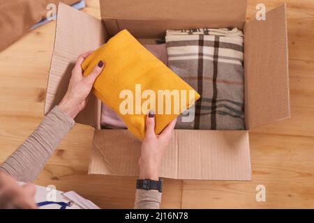 Von oben gesehen Aufnahme einer unerkennbaren jungen Frau, die saubere Kleidung für wohltätige Zwecke in eine Spendenbox legte Stockfoto