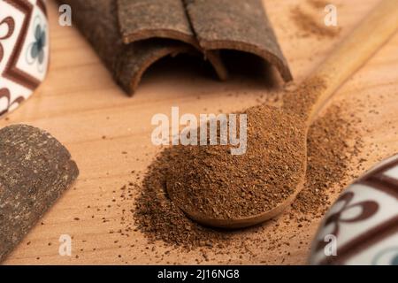 Holzlöffel gefüllt mit gemahlenem Zimt auf dem Tisch mit einigen Zimtstangen Stockfoto