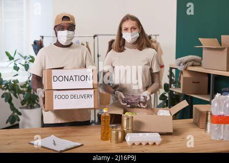 Mittleres Porträt eines jungen erwachsenen Mannes und einer jungen Frau, die Schutzmasken und Handschuhe tragen und in wohltätiger Zusammenarbeit mit Blick auf die Kamera arbeiten Stockfoto