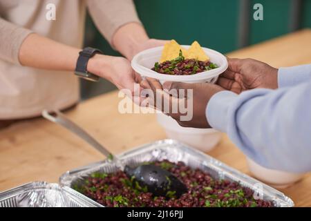 Mittlere Nahaufnahme eines nicht erkennbaren Freiwilligen, der den Begünstigten in der Kantine der Wohltätigkeitsorganisation Teller mit Essen übergab Stockfoto